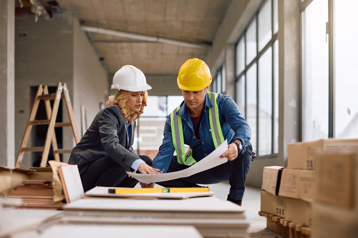 Construction worker and developer collaborating while examining construction plans at a building site